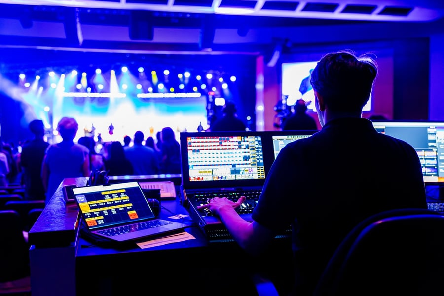 A lighting operator at a front-of-house desk, blue-lit venue beyond