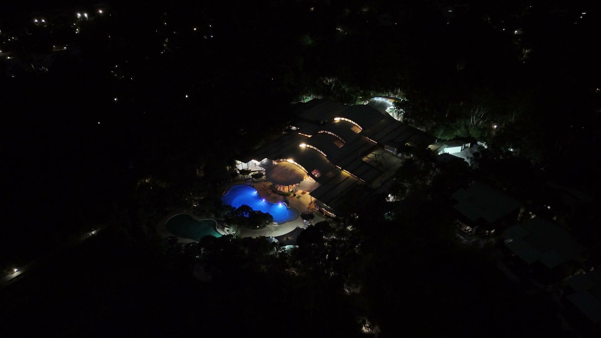 Aerial night view of a lit resort with a glowing pool