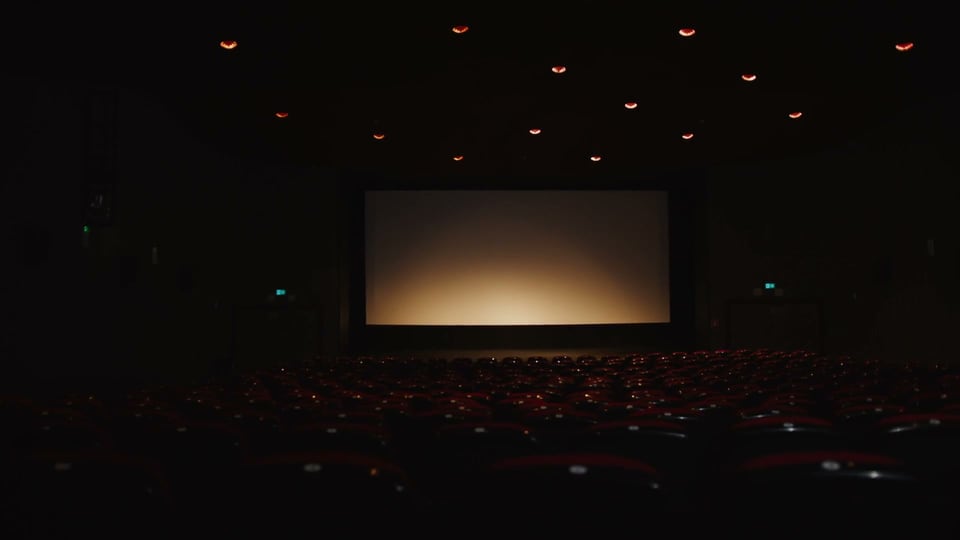 Empty auditorium, amber safety lights, a glowing screen far ahead