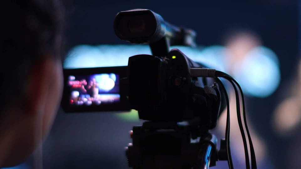A camcorder monitor over an operator's shoulder in blue studio light