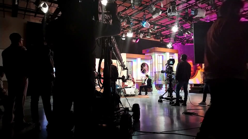 A TV studio floor in silhouette, crew and pedestal cameras